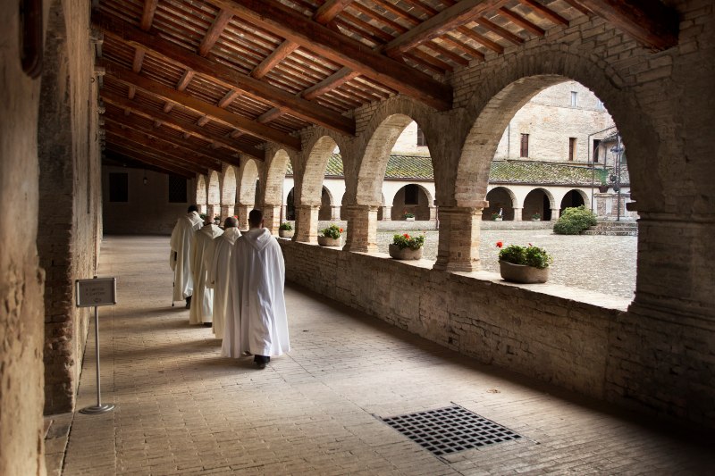 chiostro dell'abbazia di Fiastra con monaci in cammino in primo piano 